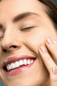 A close-up portrait of a joyful woman with closed eyes, pink lipstick, and her hand touching her cheek.