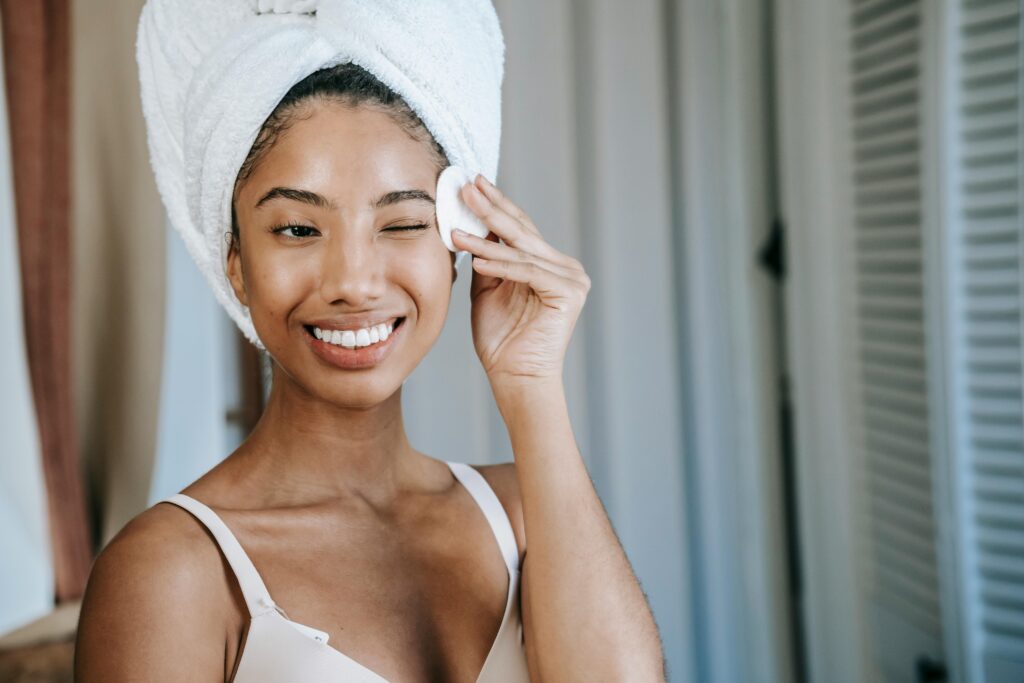 A cheerful woman cares for her skin with a cotton pad, promoting healthy hygiene.