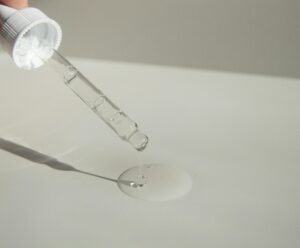 Close-up of a cosmetic pipette releasing serum onto a surface with soft sunlight.