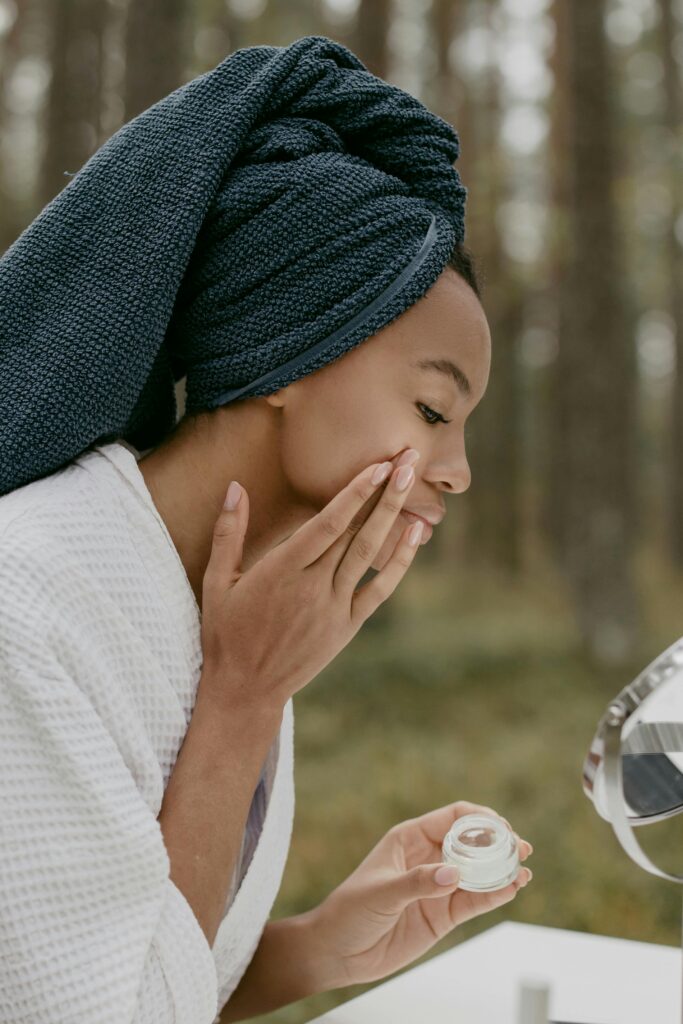 Woman enjoying a skincare routine in a forest setting, applying cream with serene focus.