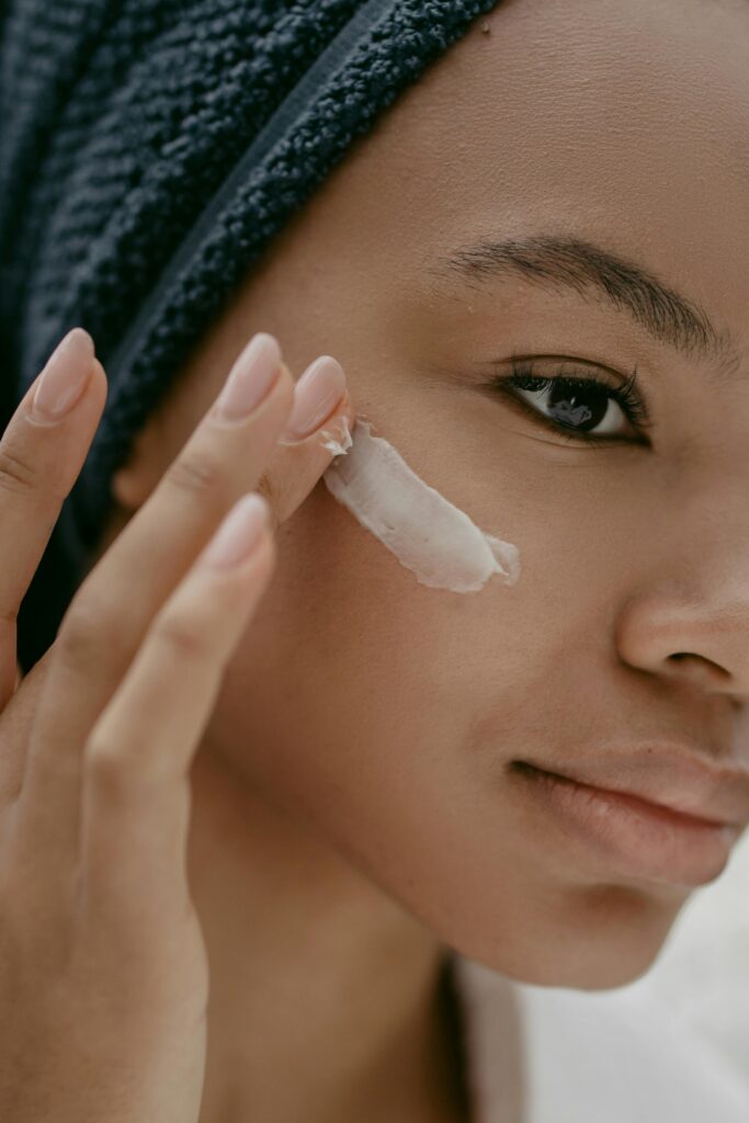 A woman gently applies moisturizing cream to her cheek, promoting healthy skin care.