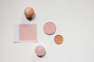 Minimalist flat lay featuring makeup products and marble spheres on a white surface, ideal for beauty and design concepts.