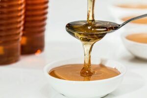 Delicious honey pouring slowly from a spoon into a white bowl, highlighting its golden hue and viscosity.