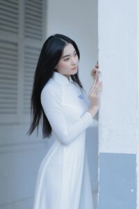 Portrait of an Asian woman in a white dress, elegantly posing indoors.