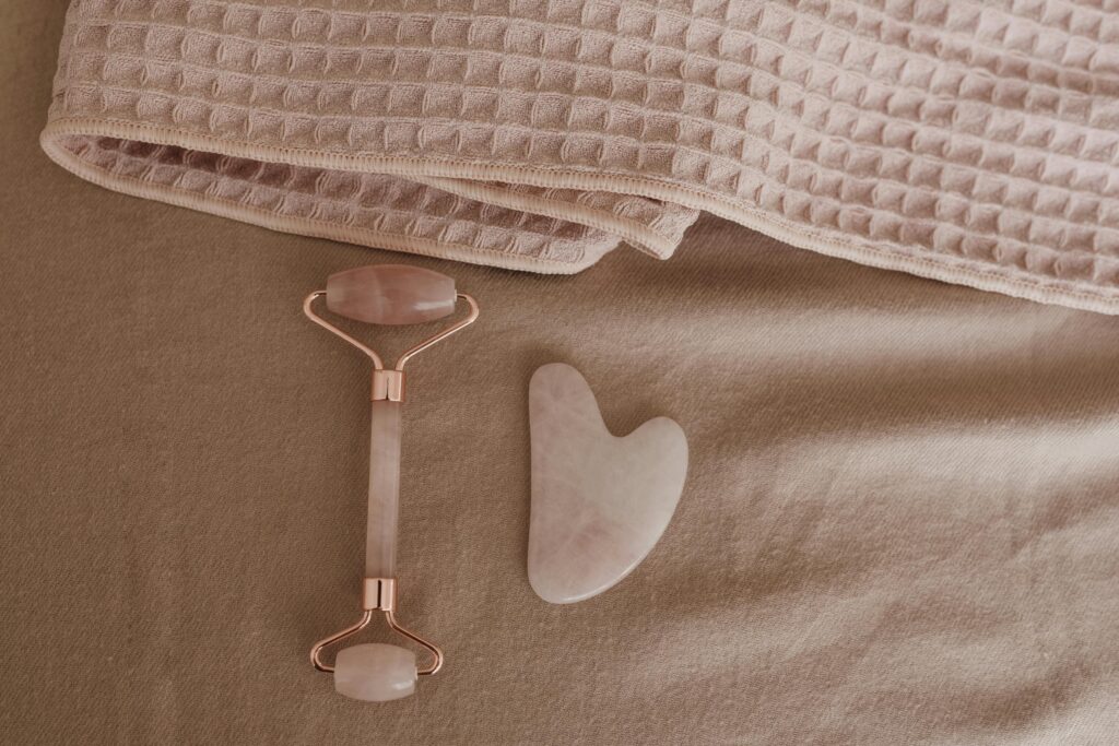 A flat lay of a rose quartz facial roller and gua sha stone on a soft pink towel, perfect for skincare routines.