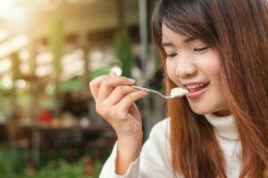 Happy woman enjoying a creamy dessert in a sunlit outdoor setting.