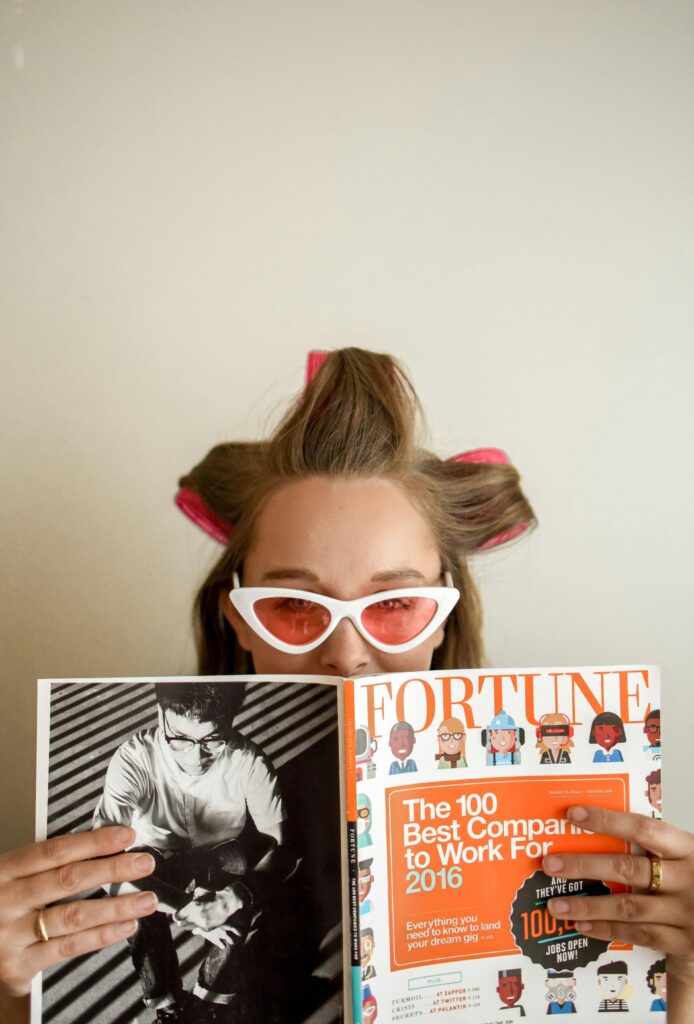 A woman with hair rollers reads a Fortune magazine, showcasing a stylish and retro look.