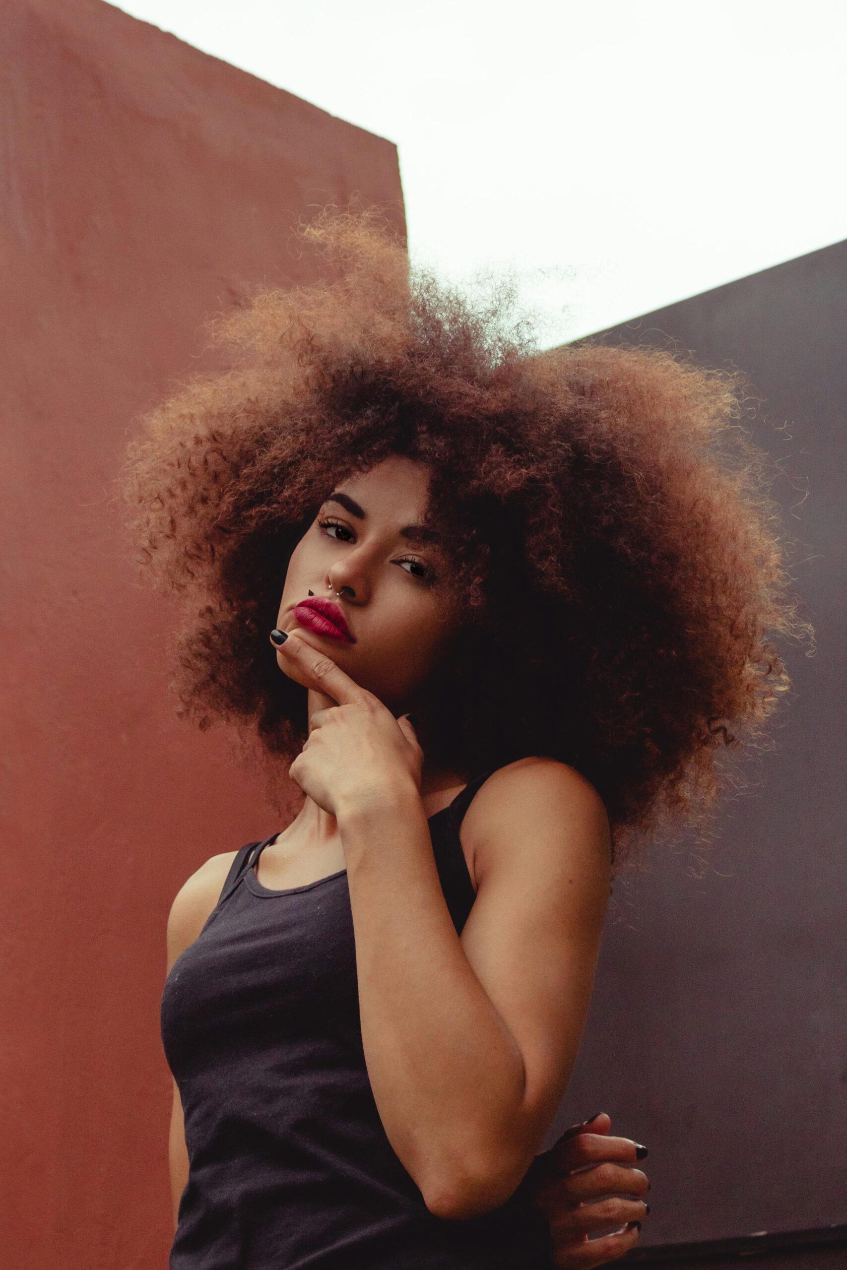 Elegant woman posing with curly hair and thoughtful expression, set against a colorful background.