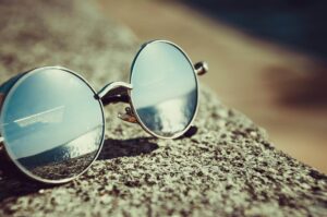 Round sunglasses resting on a sandy beach reflecting the ocean view.