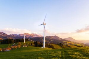 A wind turbine stands tall against a mountainous backdrop under a vibrant sky at sunset.