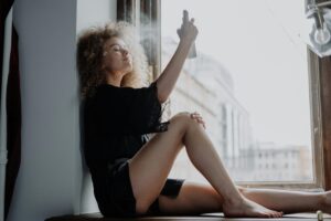 Young woman relaxing by a window while applying hydrating spray, enjoying a tranquil moment.