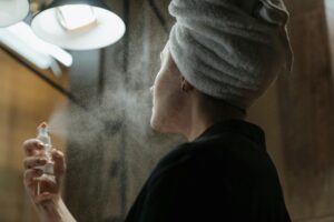 Woman with a towel on head applying facial spray in bathroom, focusing on skincare and self-care.