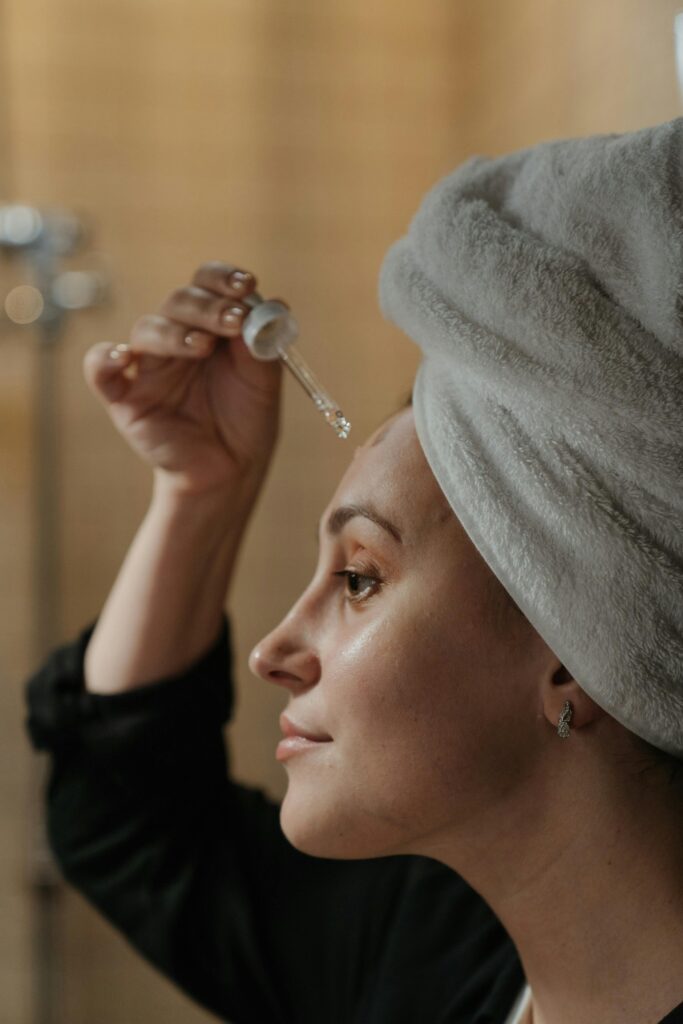 Close-up side view of a woman applying skincare serum with a dropper, promoting beauty routine.