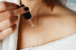 A woman applying skin care oil to her collarbone area for self-care treatment.